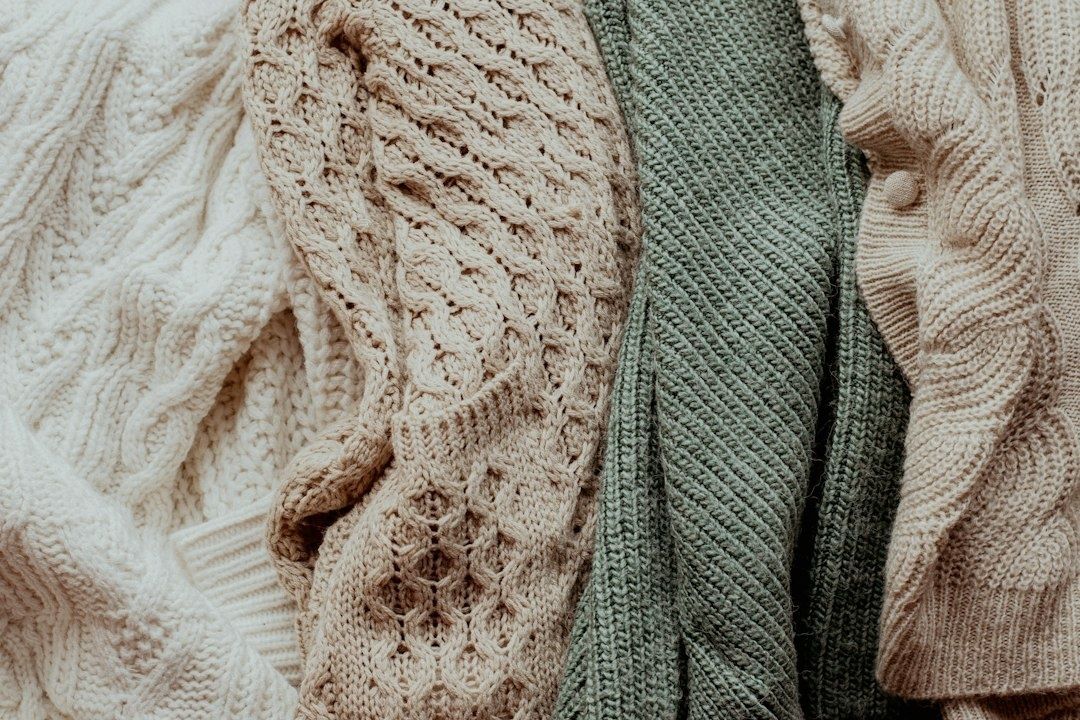Nahaufnahme mehrerer gestrickter Pullover in Wolltönen und Salbeigrün
